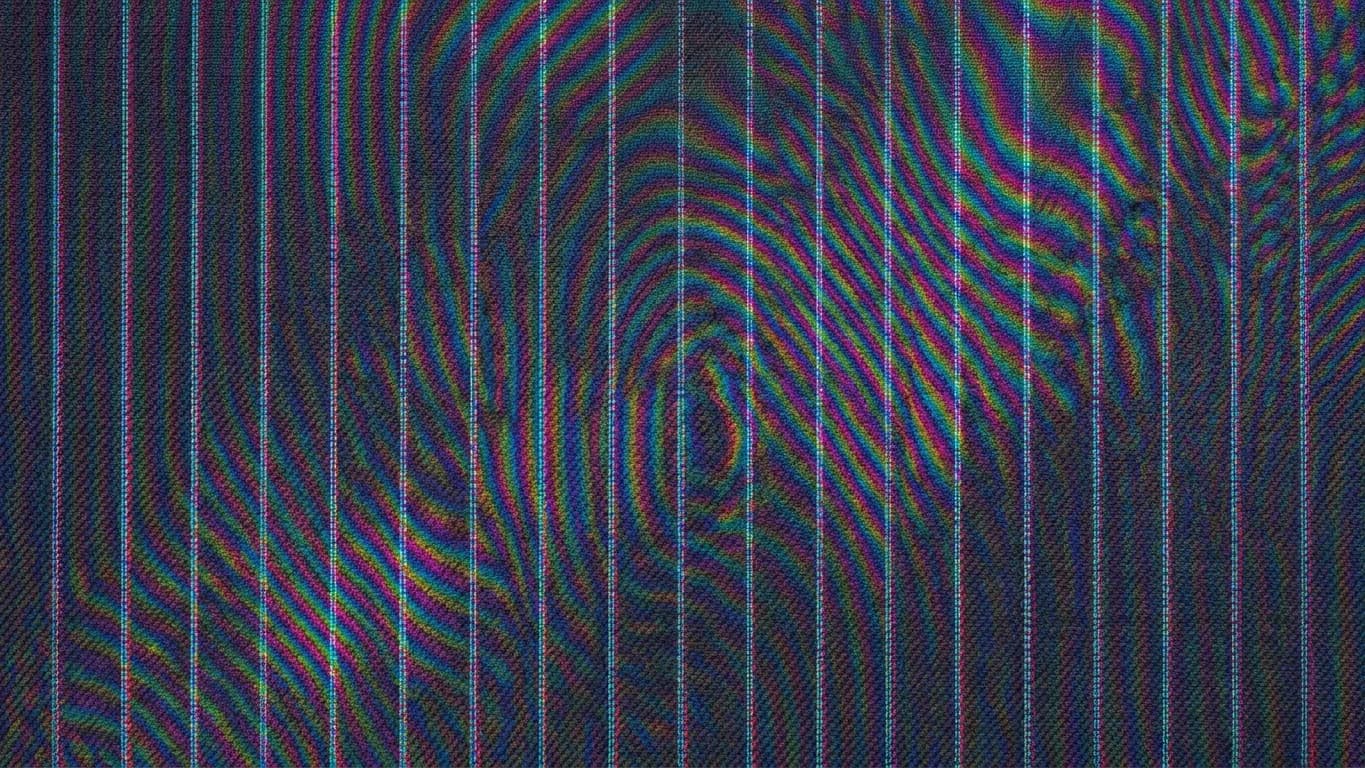 The identical cloth as a sensor records it: broad rainbow interference bands curve across the stripes in concentric arcs, magenta and green, sitting on top of the weave rather than in it.