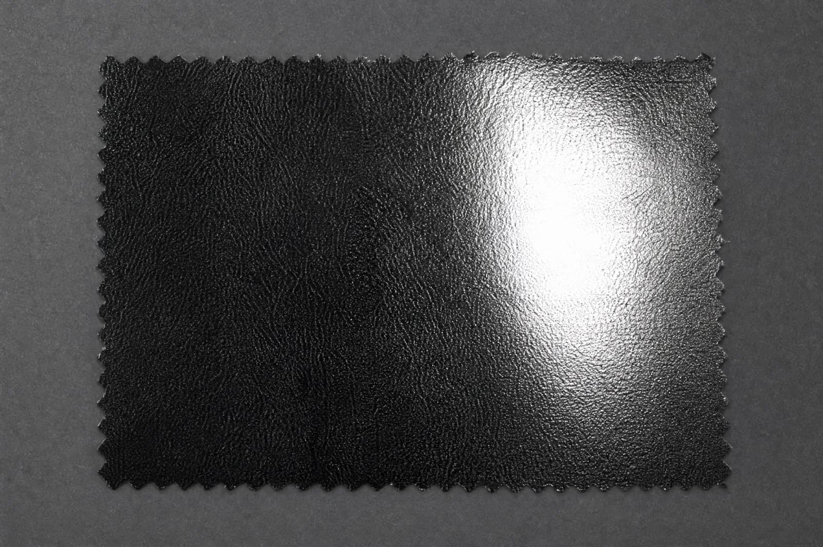 A glossy coated black surface with one broad blown-out highlight erasing the texture underneath.