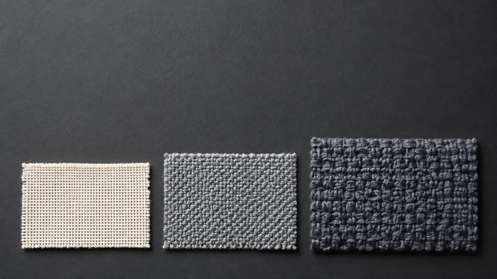 Three rectangular cloth swatches of increasing complexity arranged as a stepped row on a graphite surface.